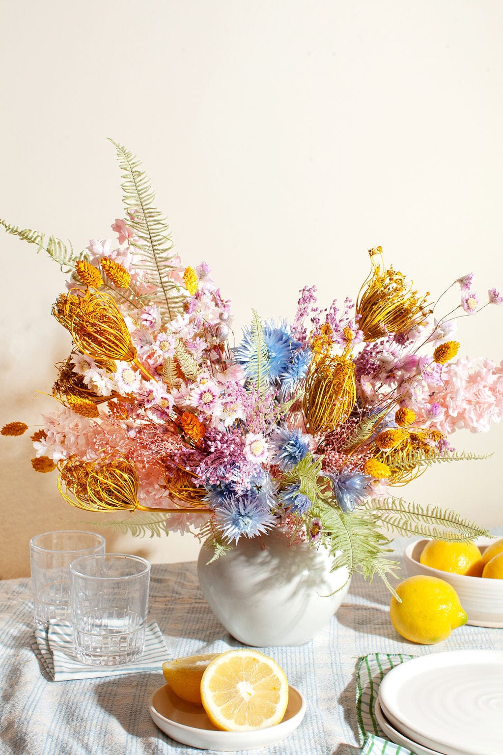 Decorative floral arrangement with pastel flowers and greenery on a table with lemons and glasses.